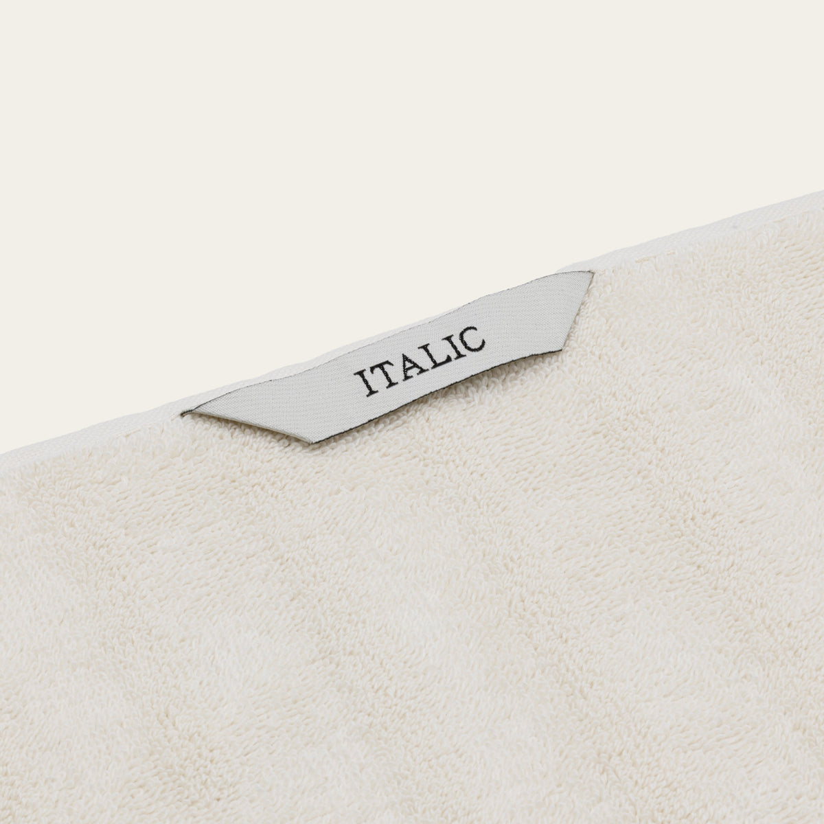 Off-white cotton towel with stitched label reading “ITALIC” on textured surface