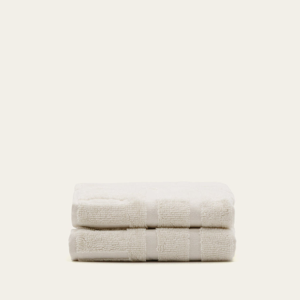Two folded off-white cotton towels with subtle stripe bands and plush terry loops