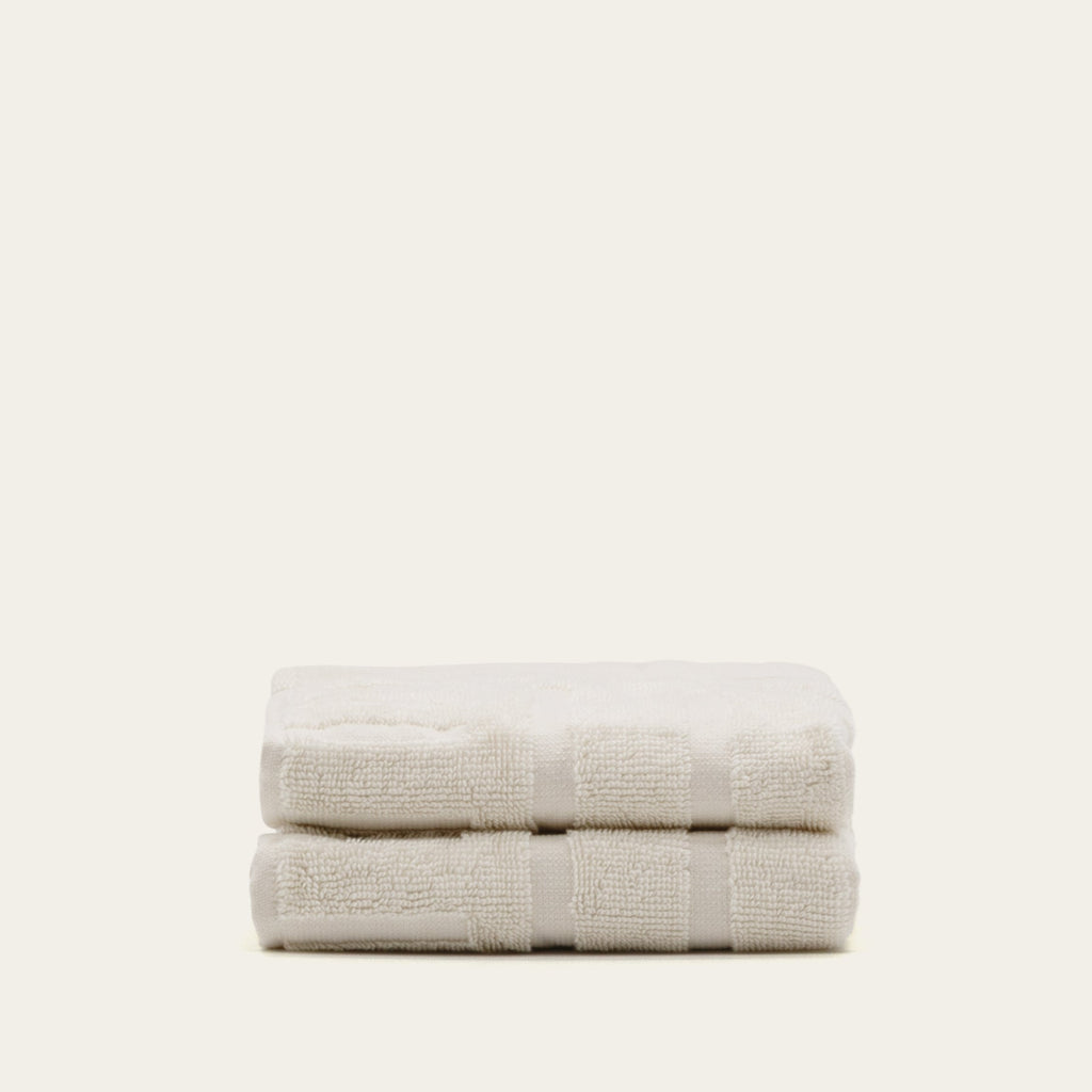 Two folded cream cotton towels with woven stripe detail