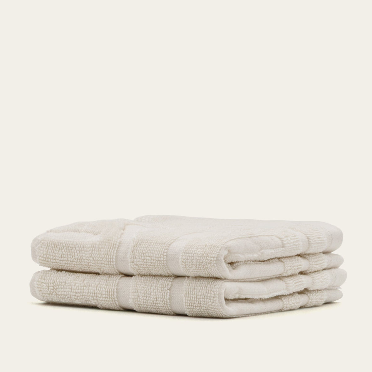 Ecru cotton bath towels stacked, showing terry texture and folded seam