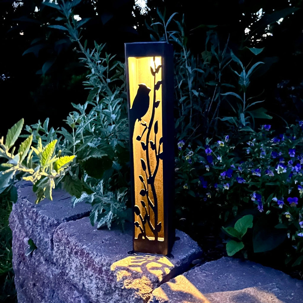 Steel solar garden luminary pillar with cardinal cutout, warm light glowing