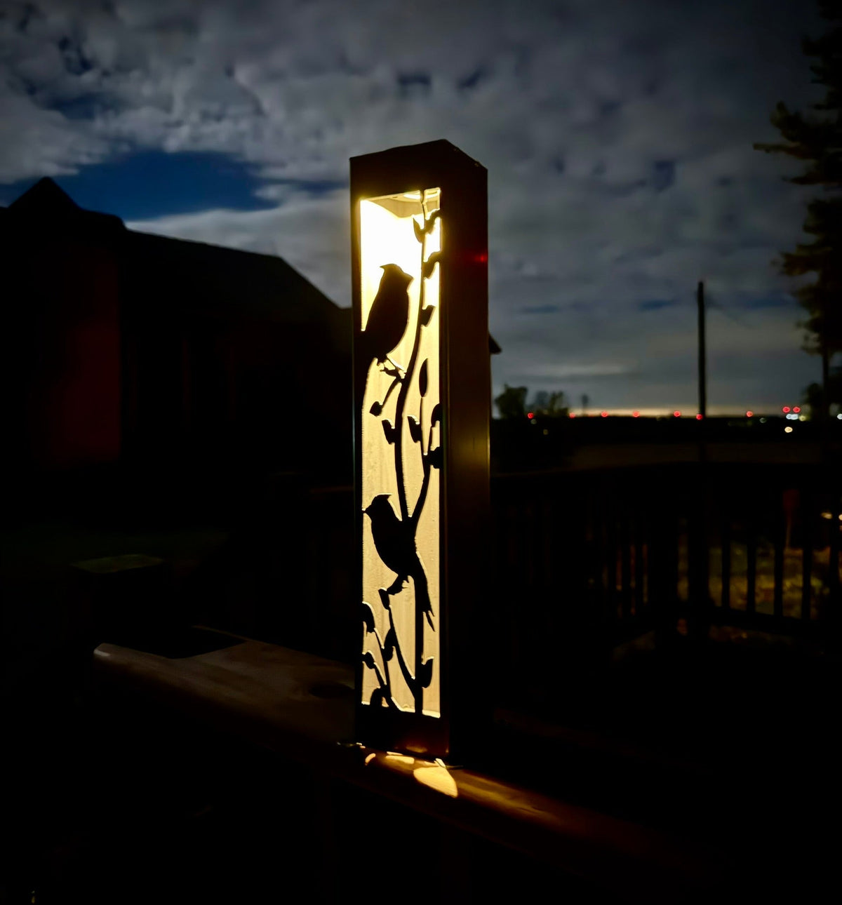 Steel solar garden luminary pillar with cardinal silhouette, glowing warm light