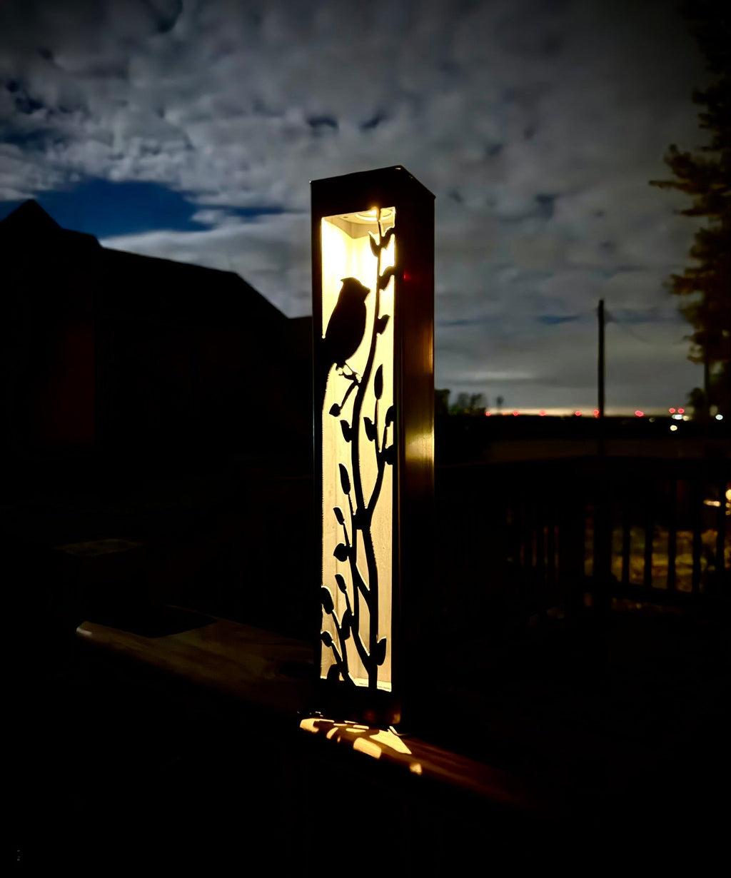 Steel solar garden luminary pillar with cardinal cutout, illuminated at night