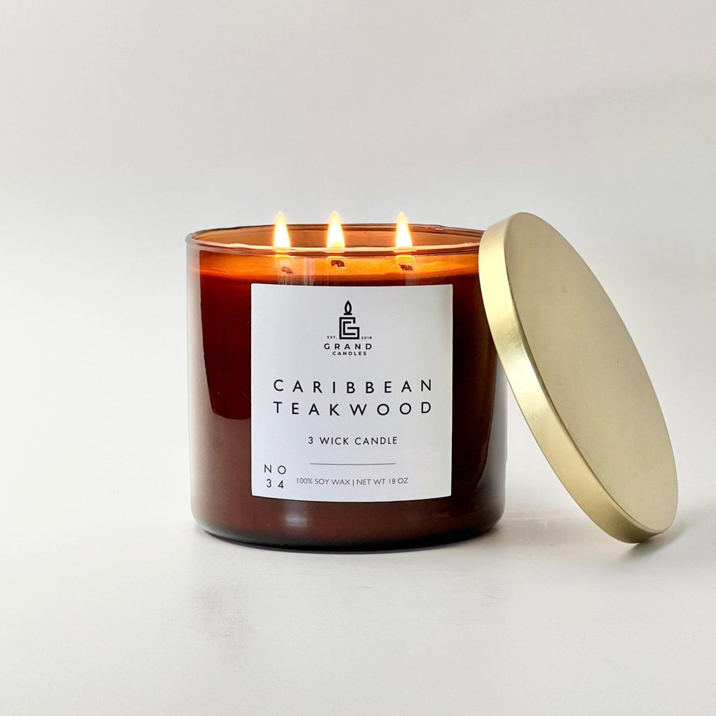 Caribbean teakwood soy candle in amber glass jar with white label and gold lid beside it.
