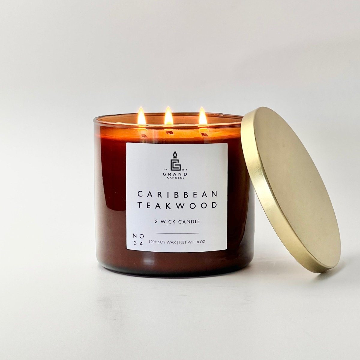 Caribbean teakwood soy candle in amber glass jar with white label and gold lid beside it.