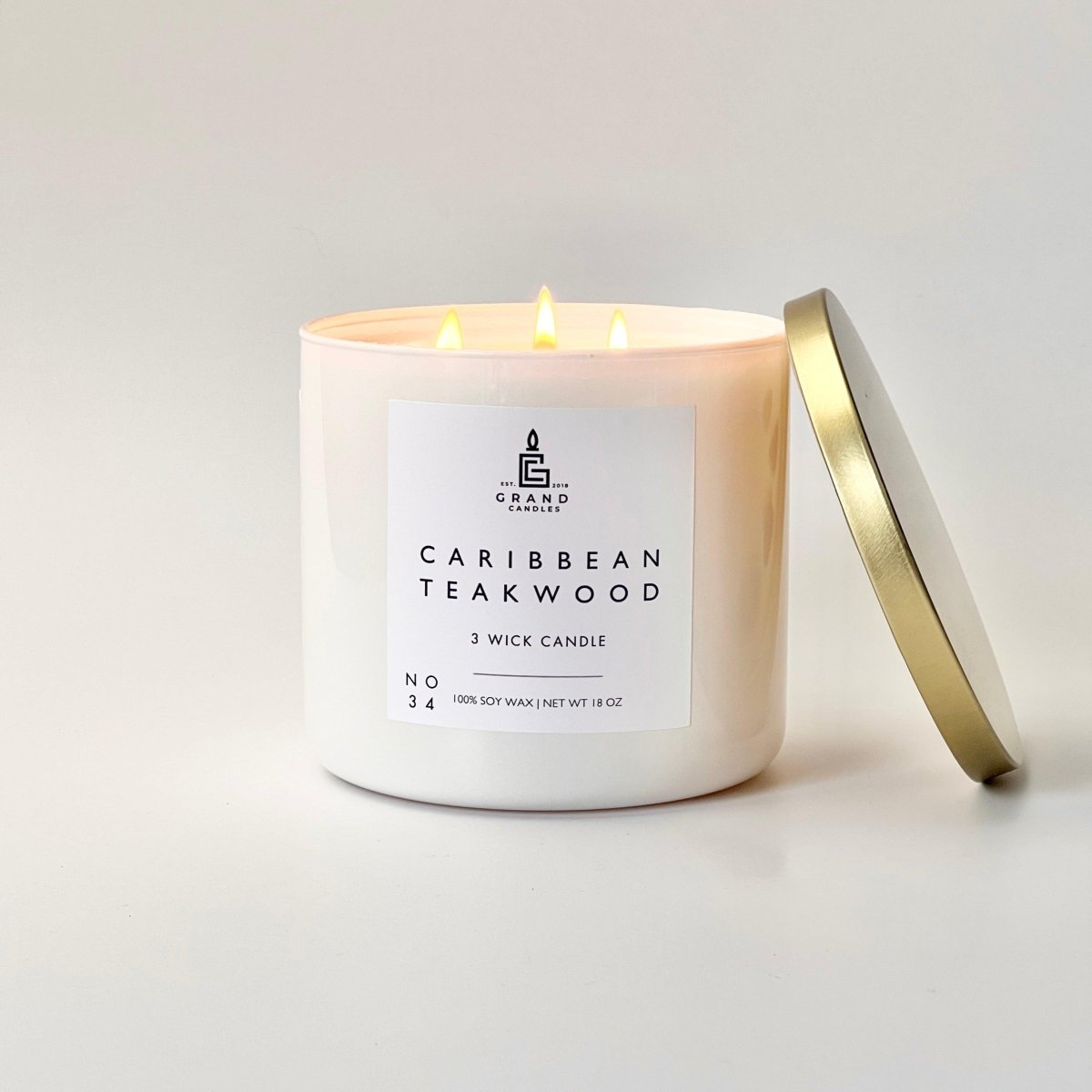 Caribbean teakwood soy candle in white wax jar with white label, gold lid resting nearby.