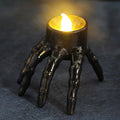 Gold skeleton hand candle lantern with one lit tealight, three legs visible
