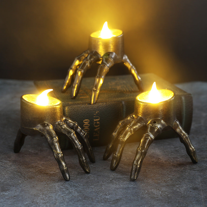 Metallic skeleton hand candle holder lantern with three lit candle flames