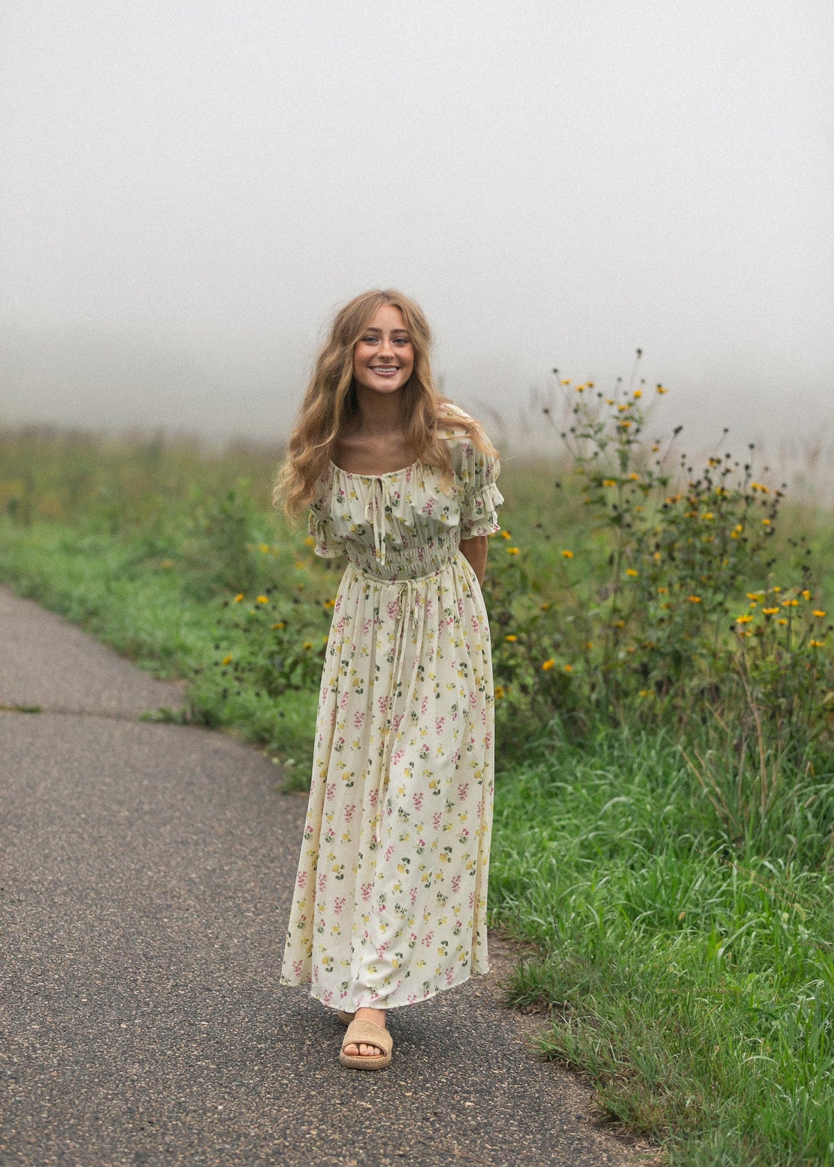 Cream floral maxi dress with puff sleeves, gathered waist, and flowing skirt on road.