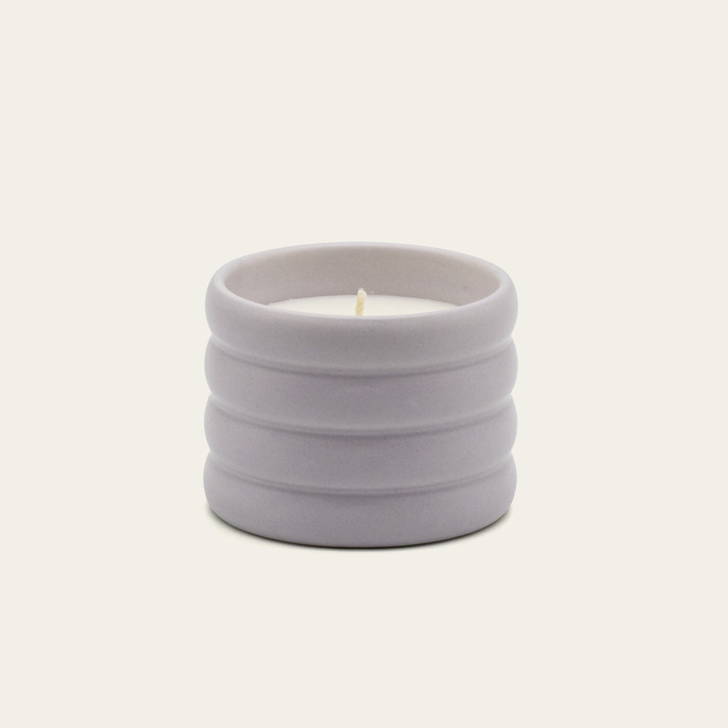Lilac ceramic soy candle with lit wick in ribbed stoneware vessel.