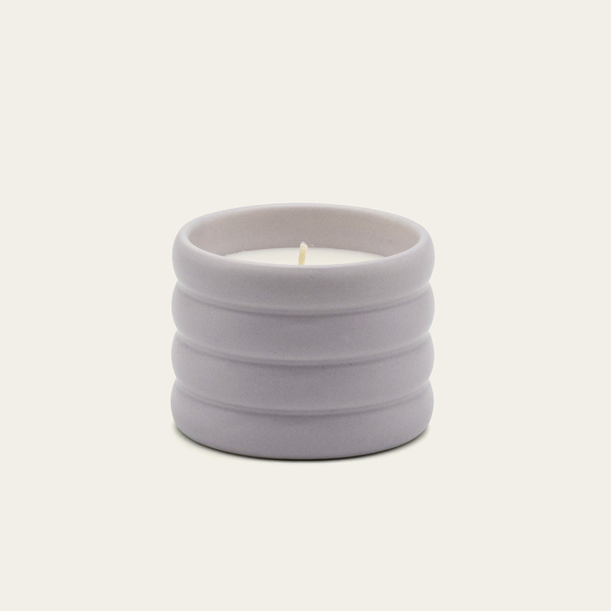Lilac ceramic soy candle with lit wick in ribbed stoneware vessel.
