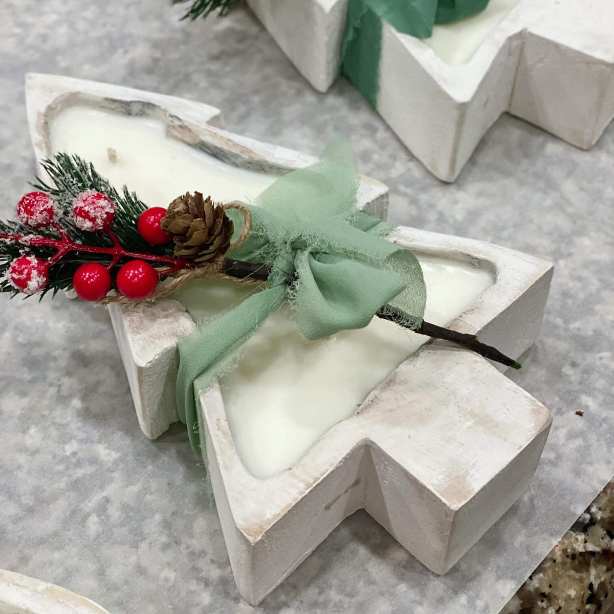White Christmas tree candle with green bow, pinecone, and red berry sprig in angled view