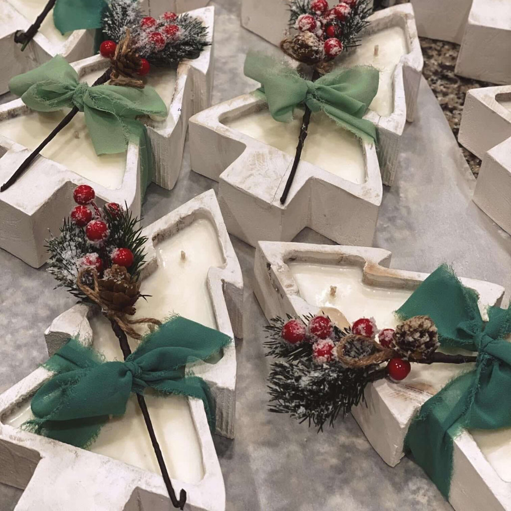 Multiple sculptural Christmas tree candles, each with green bow and red berry pinecone accents