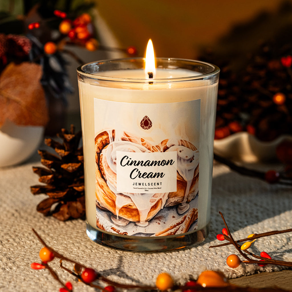 Mystery jewelry candle in clear glass, lit wick, cream cinnamon scent label
