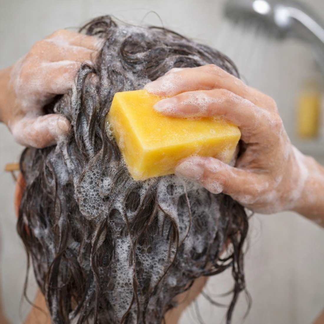 Citrus shampoo bar held to wet hair, visible foamy soap