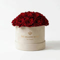 Beige dome box filled with red roses, gold logo on front