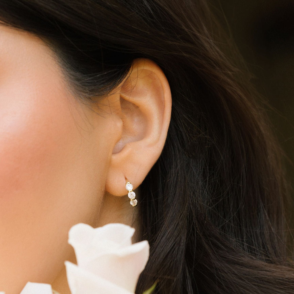 Gold-tone huggie hoop earrings with three clear stones, side ear close-up