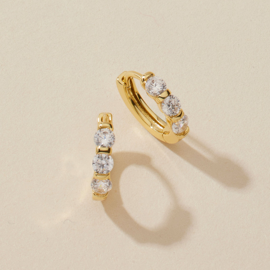 Gold-tone huggie hoop earrings with three clear stones, pair view