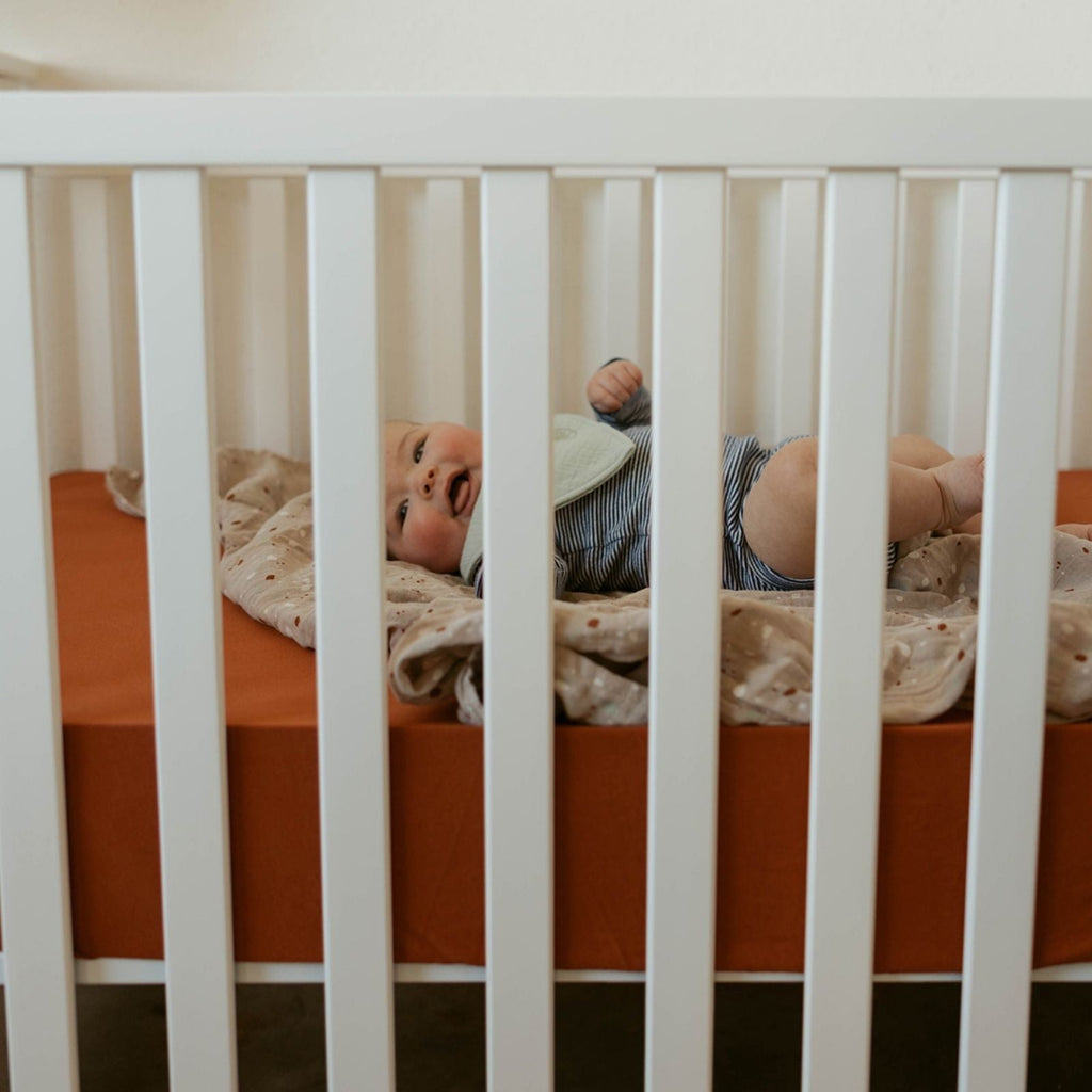 Crib sheet in a baby crib with light striped bedding and a patterned sheet panel.