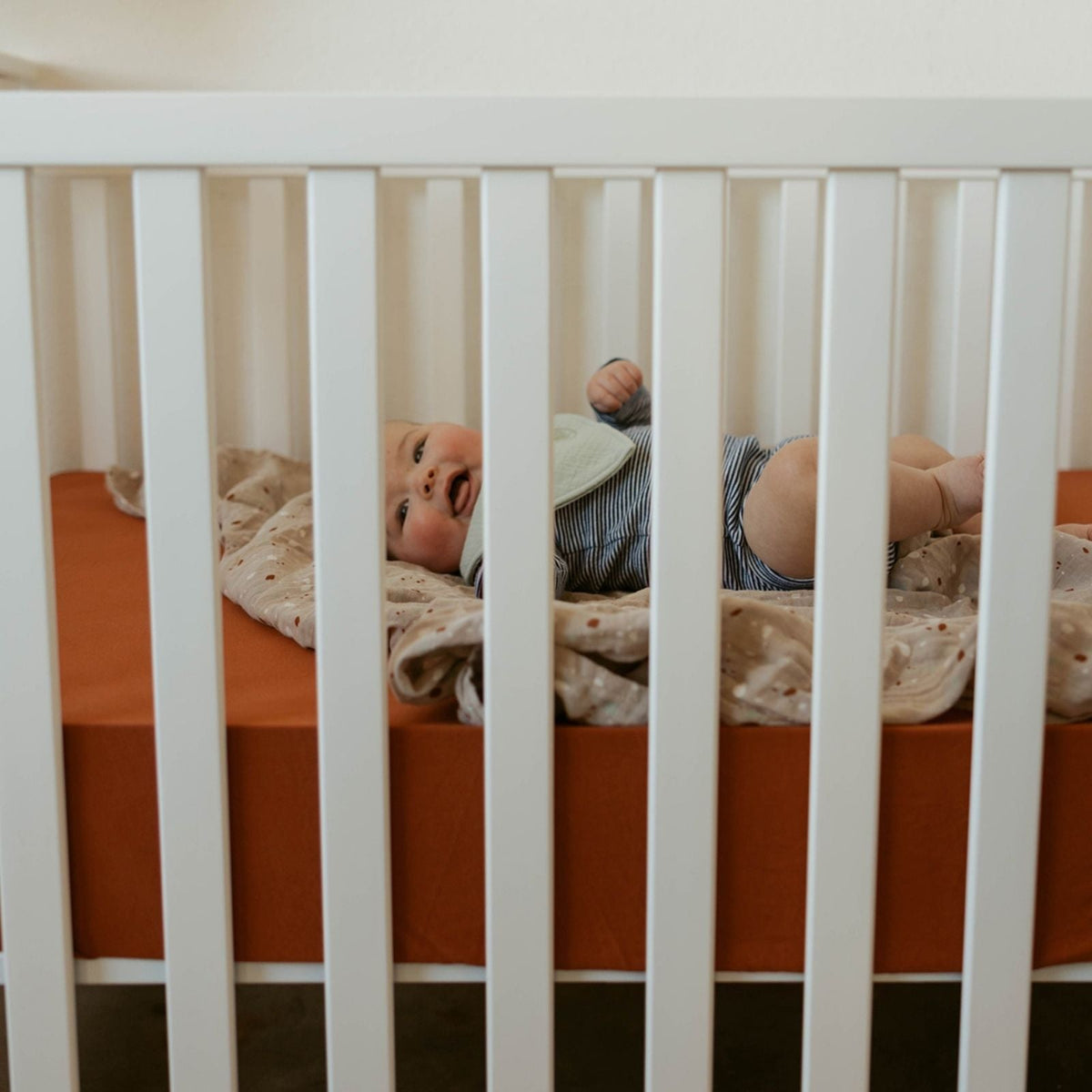Crib sheet in a baby crib with light striped bedding and a patterned sheet panel.