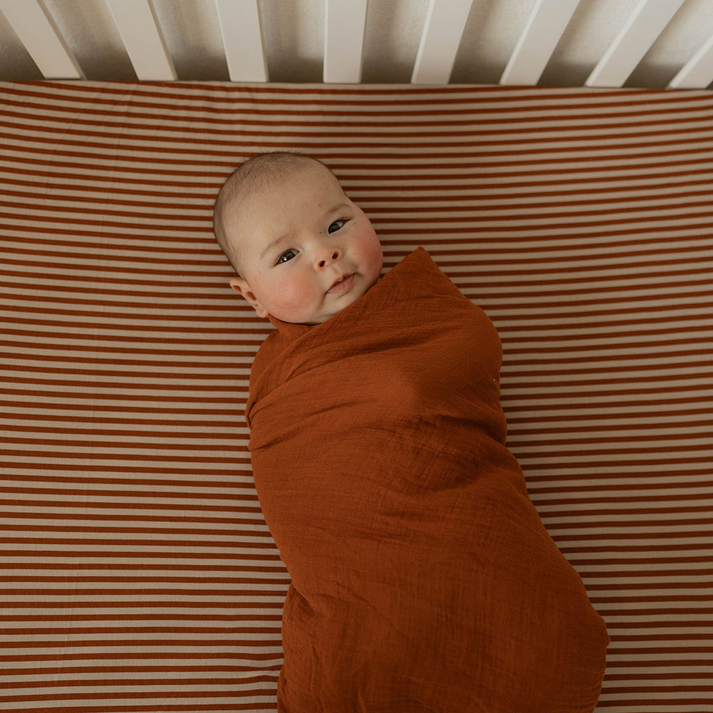 Rust-colored crib sheet with smooth fabric, fitted corner seam visible