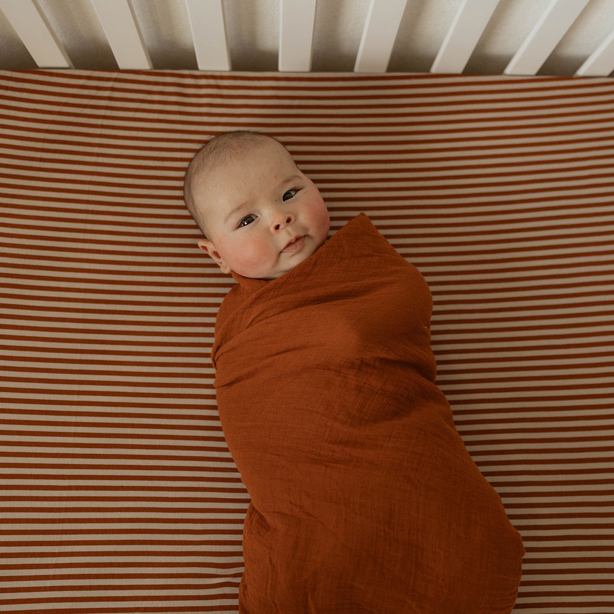 Rust-colored crib sheet with smooth fabric, fitted corner seam visible