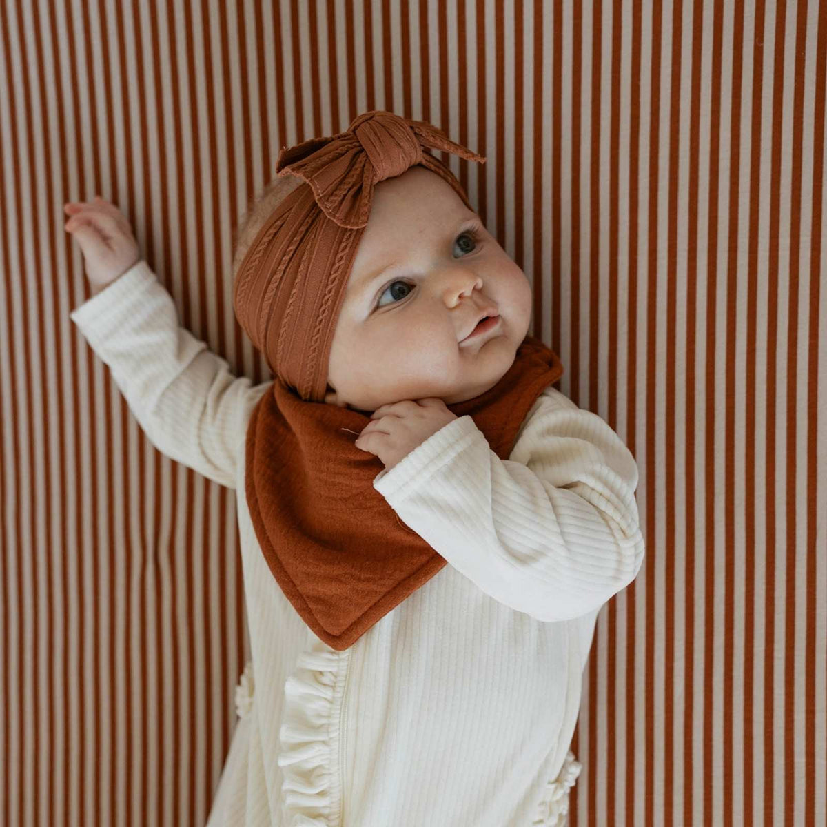 Crib sheet in warm brown fabric, shown bunched and held in front of a baby