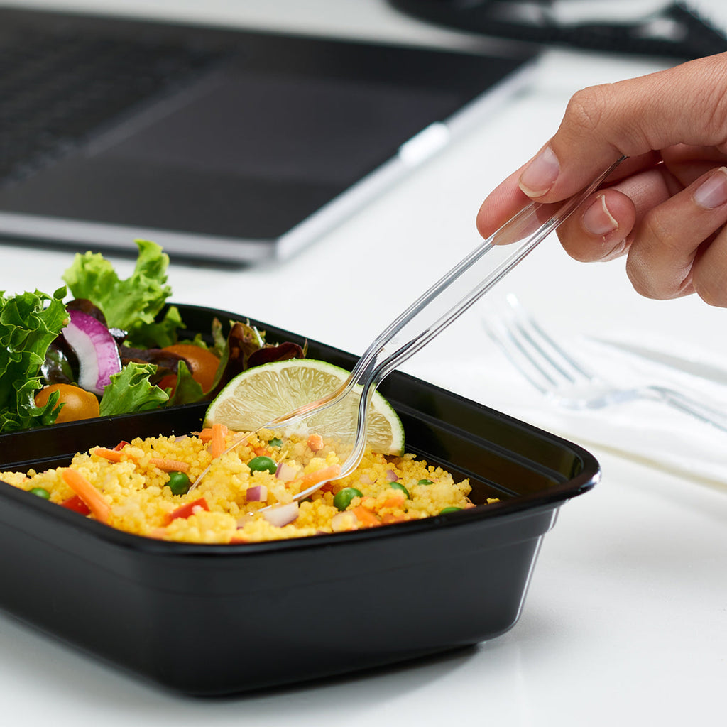 Clear plastic fork in use over a black tray meal with salad