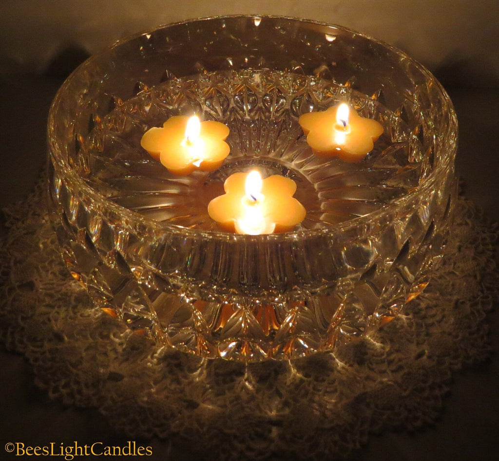 Clover-shaped yellow beeswax floating candles with flames in a glass bowl