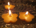 Clover-shaped yellow beeswax floating candles with flames, close-up
