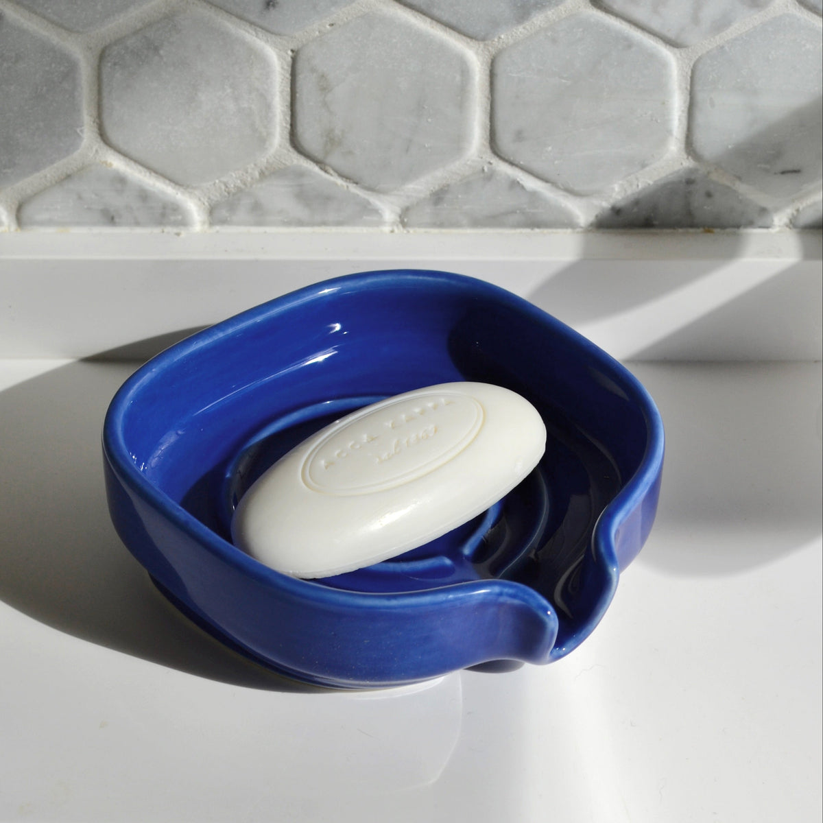 Cobalt blue porcelain soapdish holding a white bar soap in the draining well