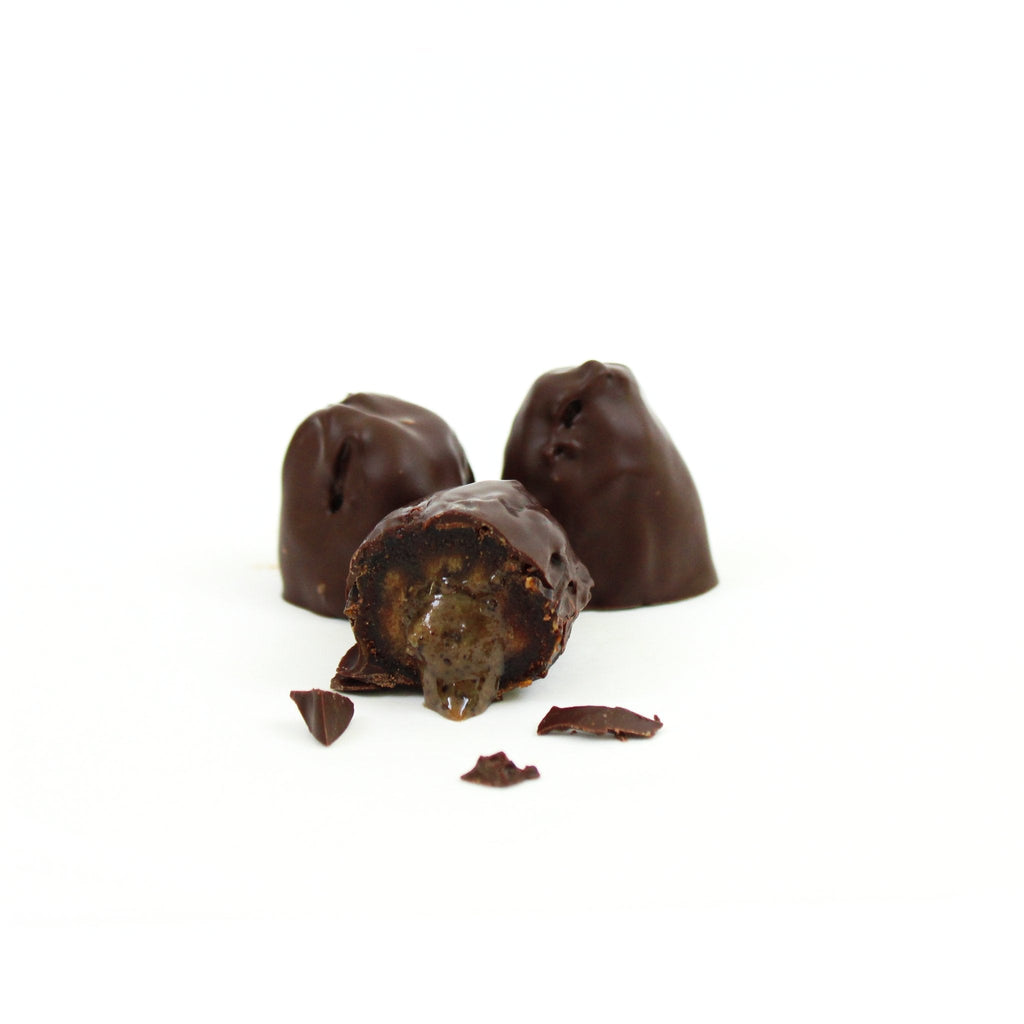Chocolate-dipped stuffed date bites with filling pieces, viewed on a clean white surface