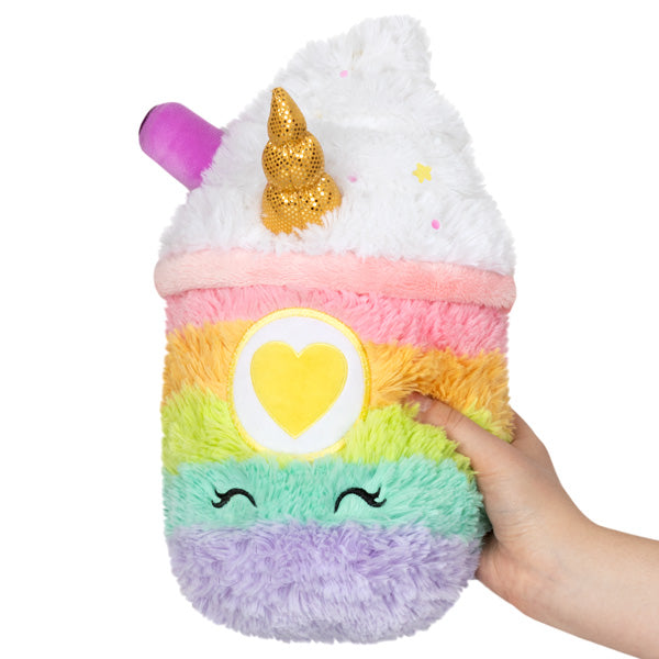 Mini plush unicorn latte with rainbow stripes and heart badge, held by hand