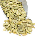 Raw pumpkin seeds in light green hulls, scattered in a metal bowl