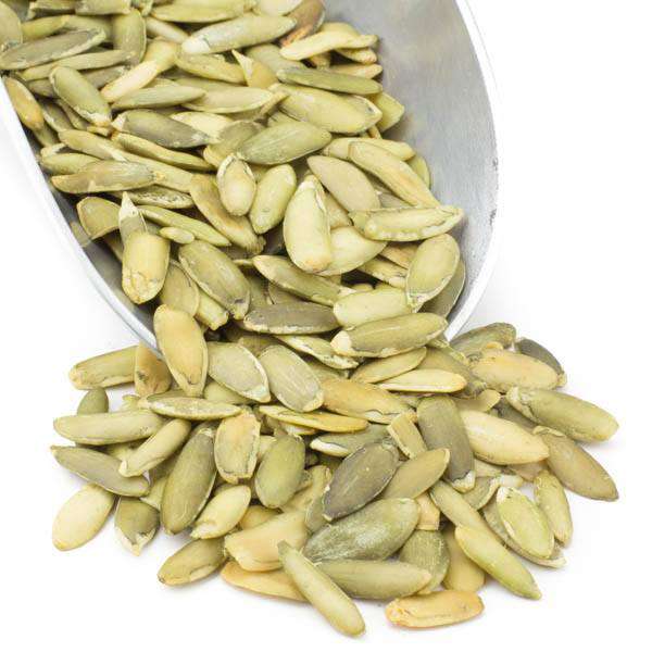 Raw pumpkin seeds in light green hulls, scattered in a metal bowl