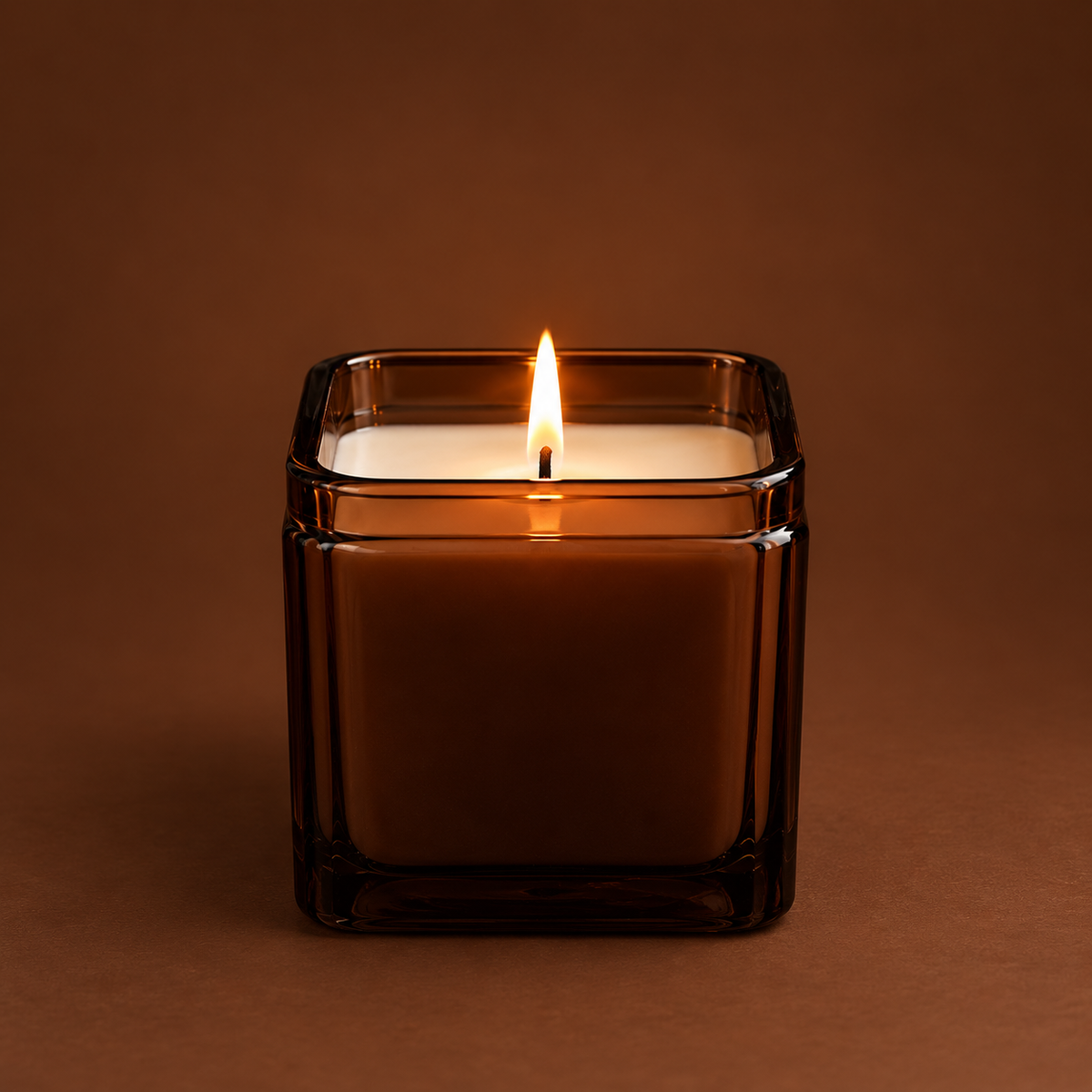 Soy jar candle in clear amber glass holder, lit flame centered on top.