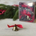 Decorative brass-tone bell with red bow ribbon on a tabletop with a clear gift box.