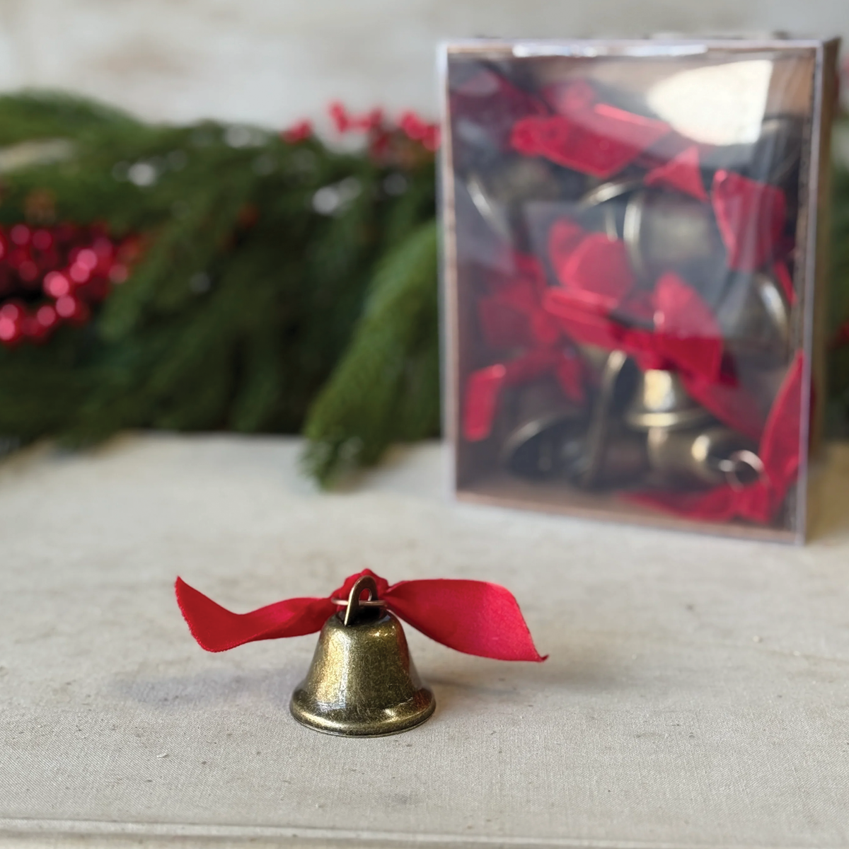 Decorative brass-tone bell with red bow ribbon on a tabletop with a clear gift box.