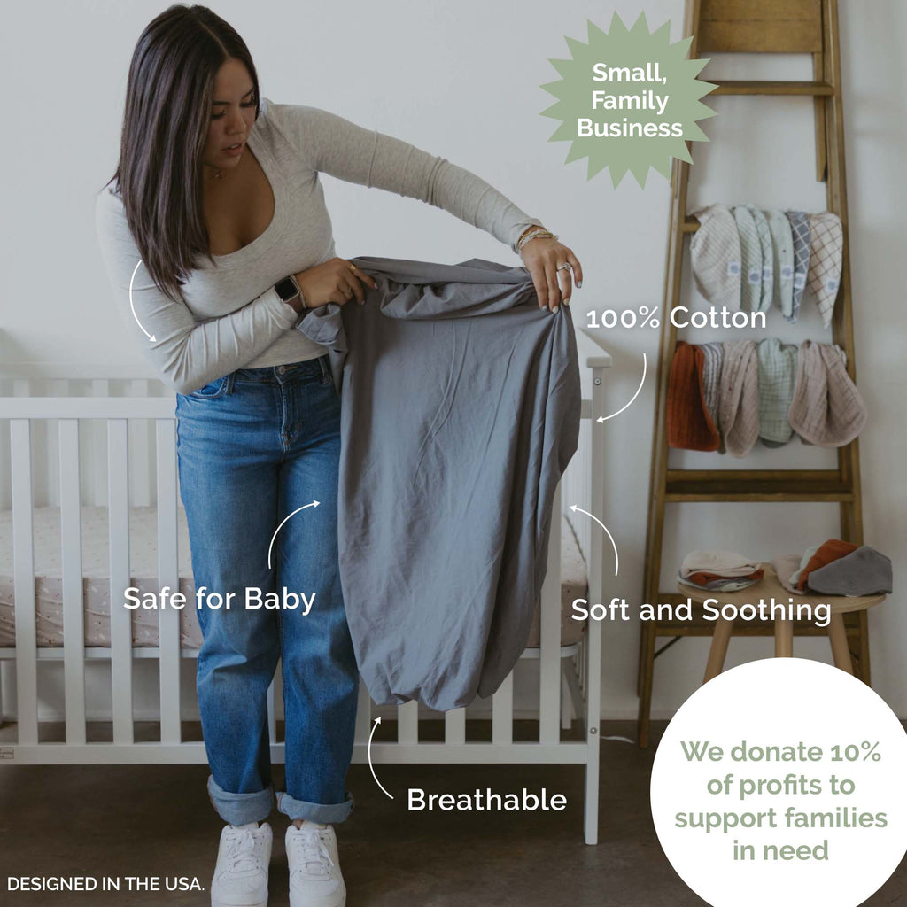 Crib sheet being held; light gray-blue fitted sheet with a smooth, solid surface.