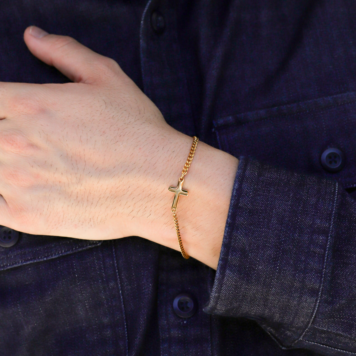 Gold cross bracelet on wrist featuring a small gold cross charm
