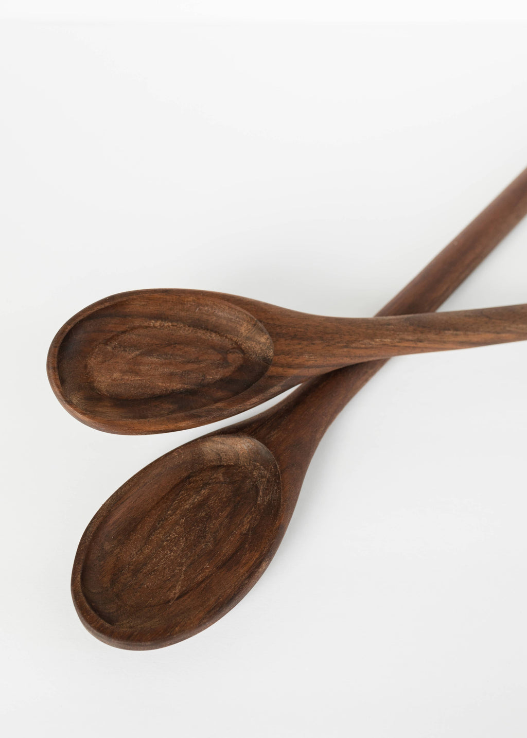 Two dark-brown wooden spoons crossed, each with an oval bowl and handle.