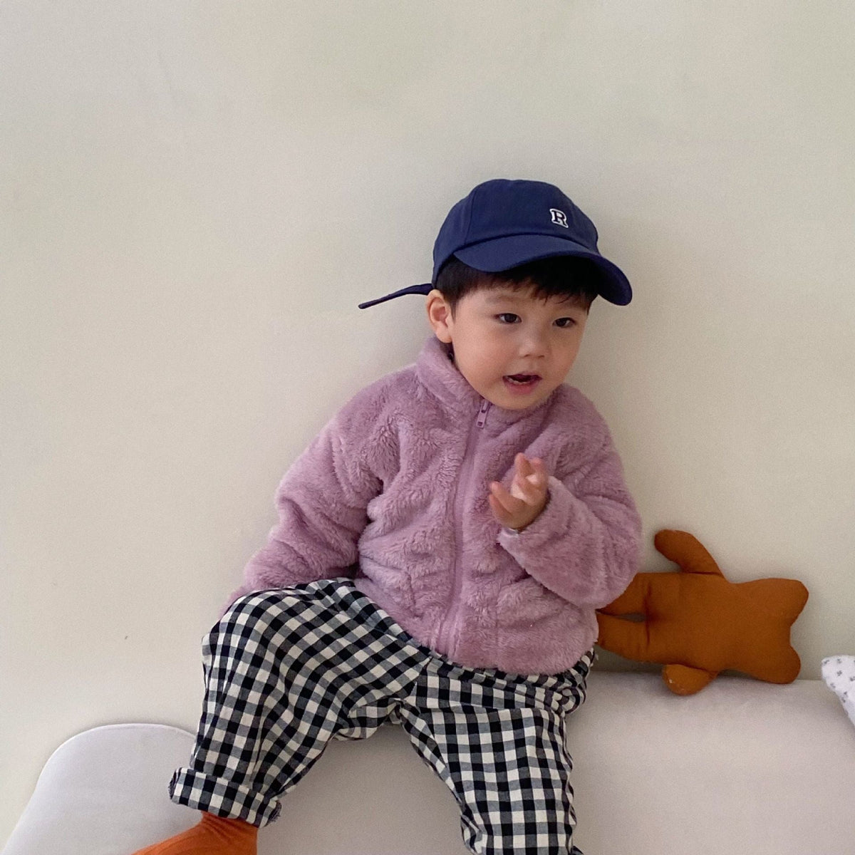 Purple kids fleece zip jacket with hood, worn with a navy baseball-style cap.