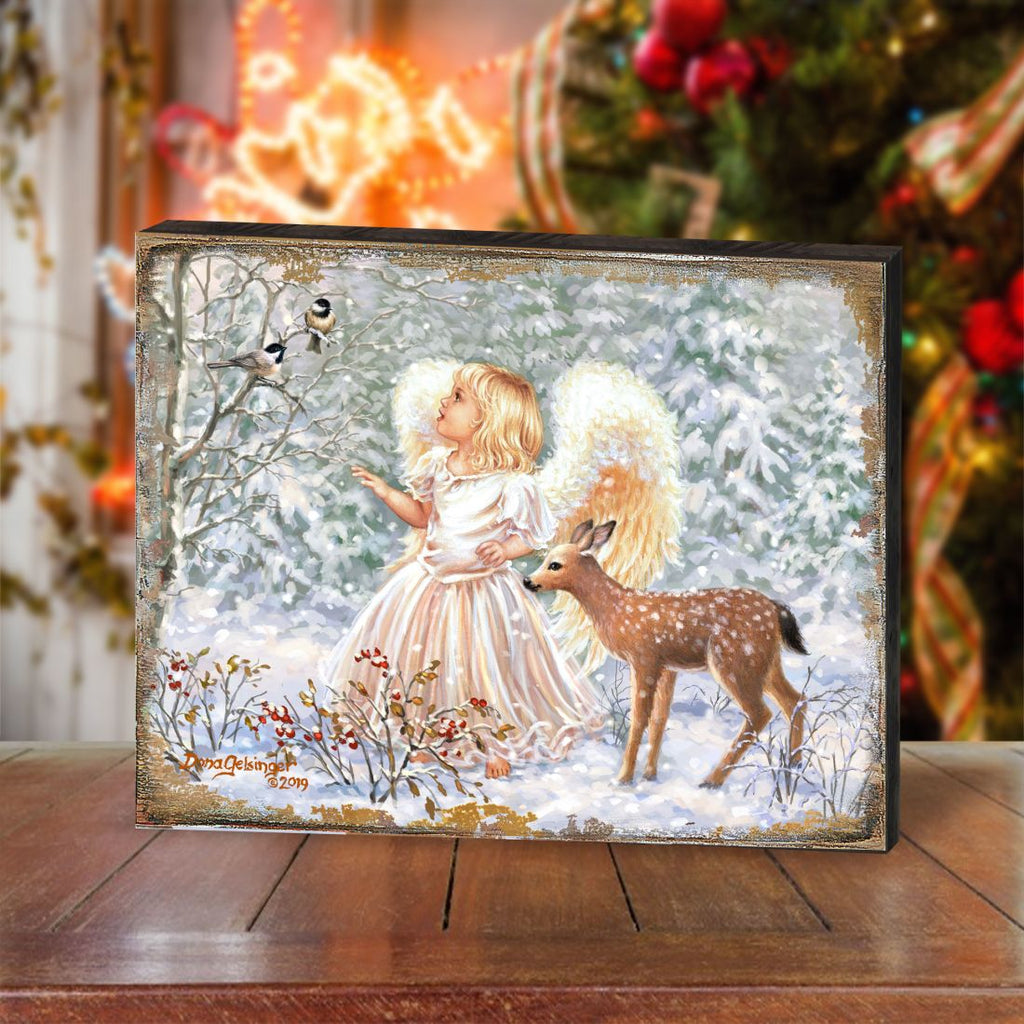 Framed wooden wall art on floor with angel girl, deer, and falling snow background