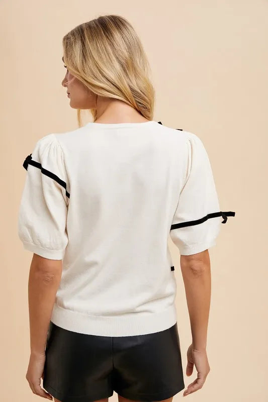 White knit top with black striped bands and bow details, shown from the back