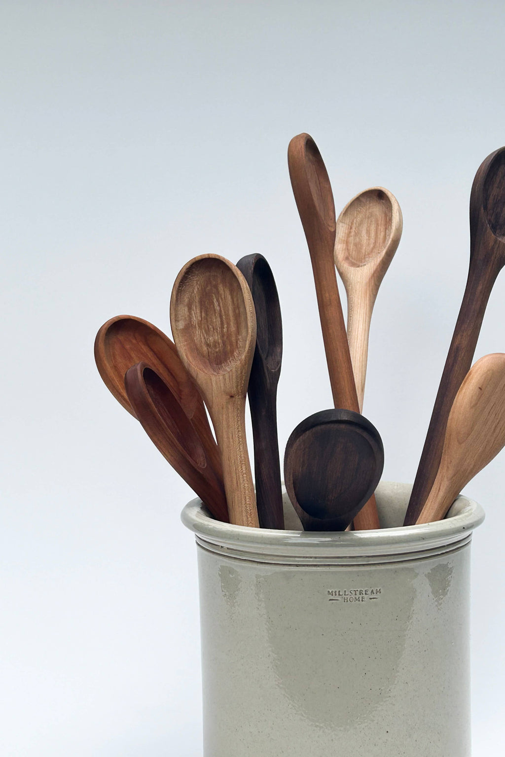 Handcrafted wooden spoons in a stoneware cup, assorted dark and light wood finishes