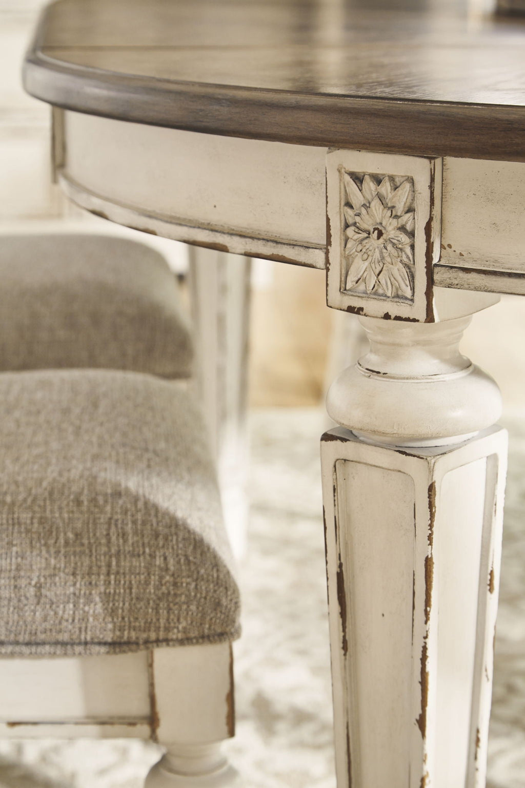 Carved white pedestal table leg with ornate panel and taupe upholstered chair seat