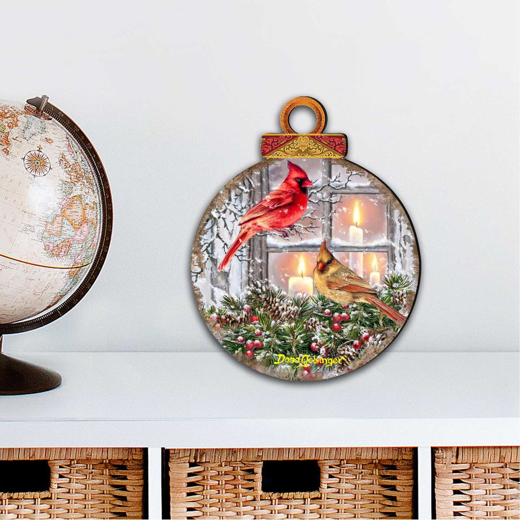 Large round outdoor ornament with red cardinal and yellow bird over lit window scene