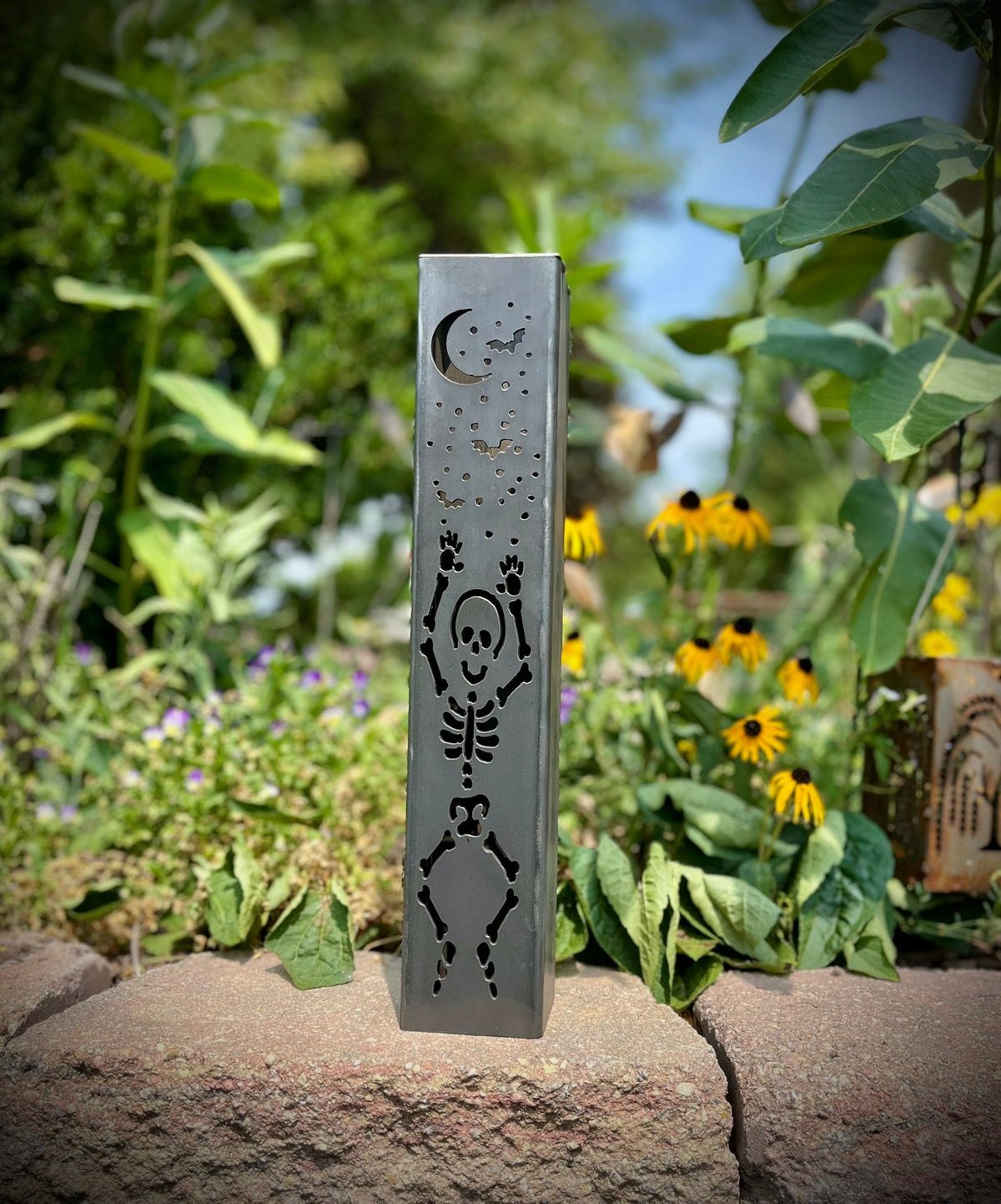 Steel solar tube light with skeleton silhouette and moon icon, installed outdoors on a stone