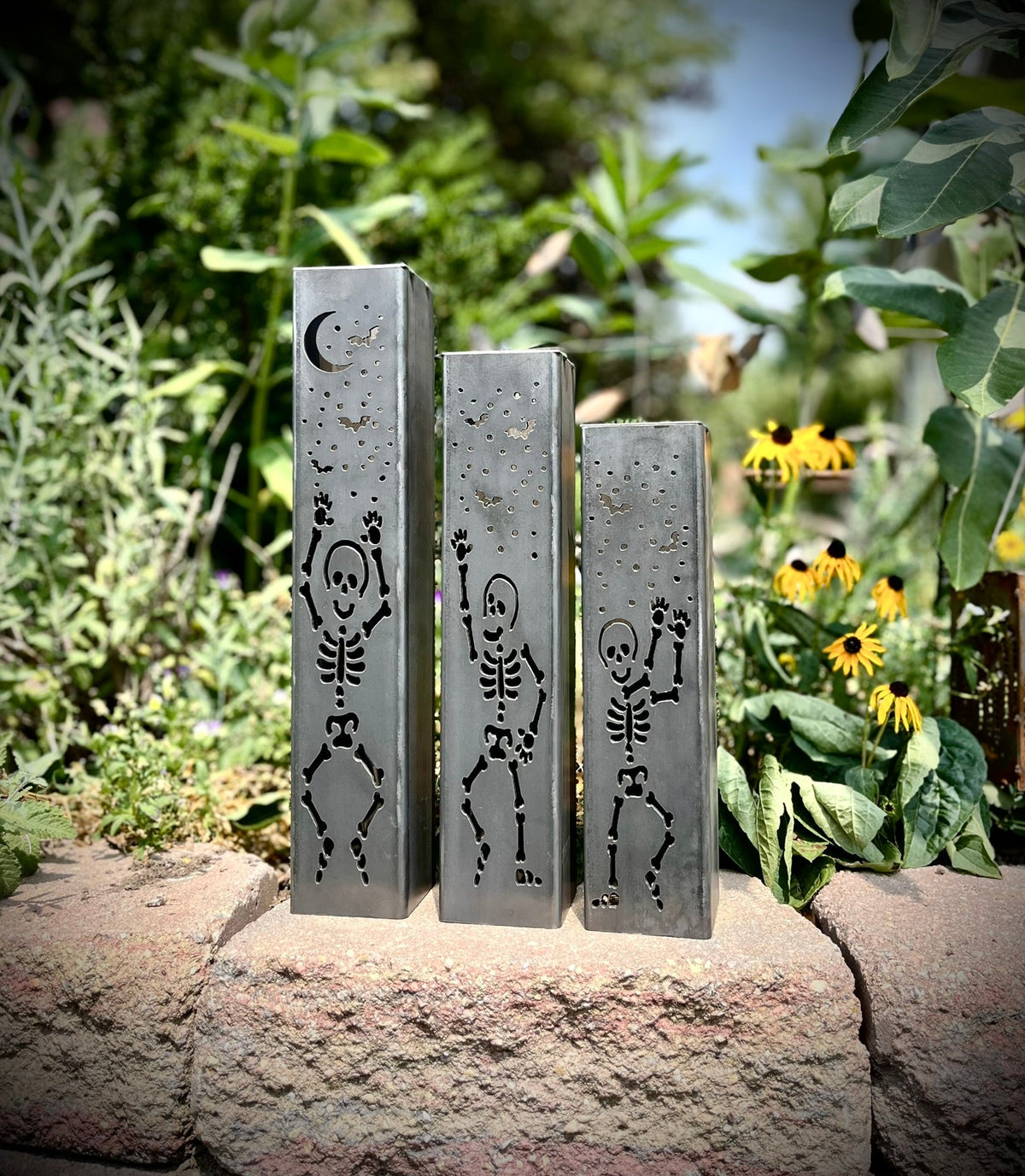 Three steel solar tube lights with skeleton silhouettes on each front panel in a garden