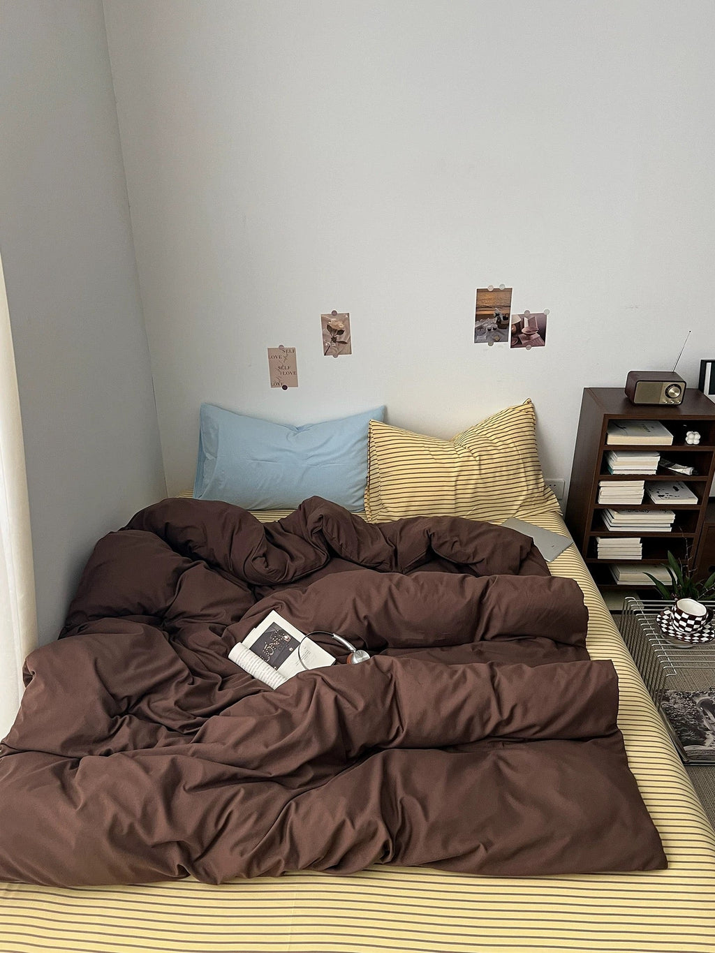 Dark brown duvet and pillowcases with yellow striped sheets and light blue accent pillow